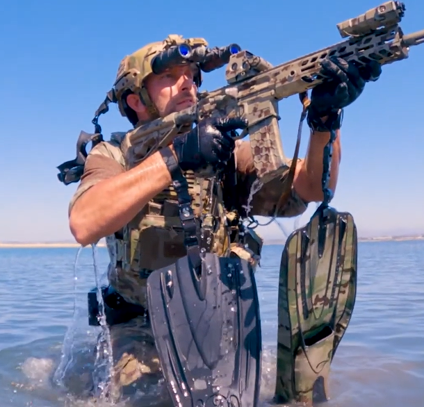 Person in tactical gear &wearing a SENTRY Gunnar Plate Carrier and holding a rifle with camouflage flippers in water 